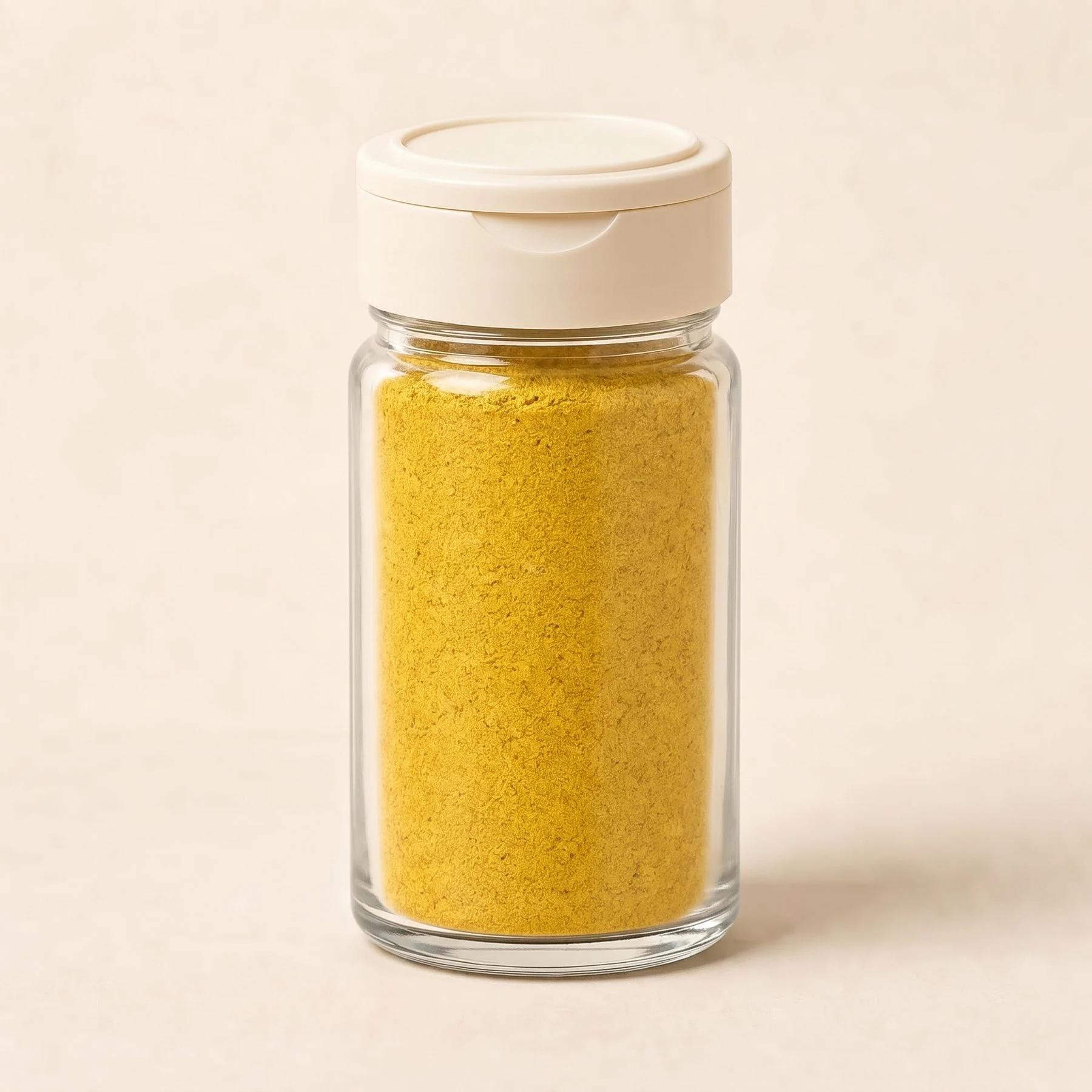 Clear glass spice jar filled with yellow seasoning and fitted with a cream plastic shaker lid